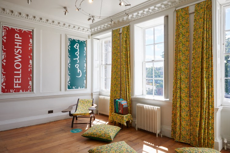 Chairs, cushions and drapes, all in the same textile pattern can be seen on wooden floors at William Morris Gallery, with light coming through the window.
