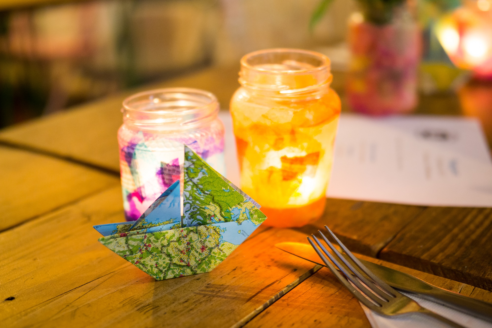 A table lit with candles, with a paper origami ship.