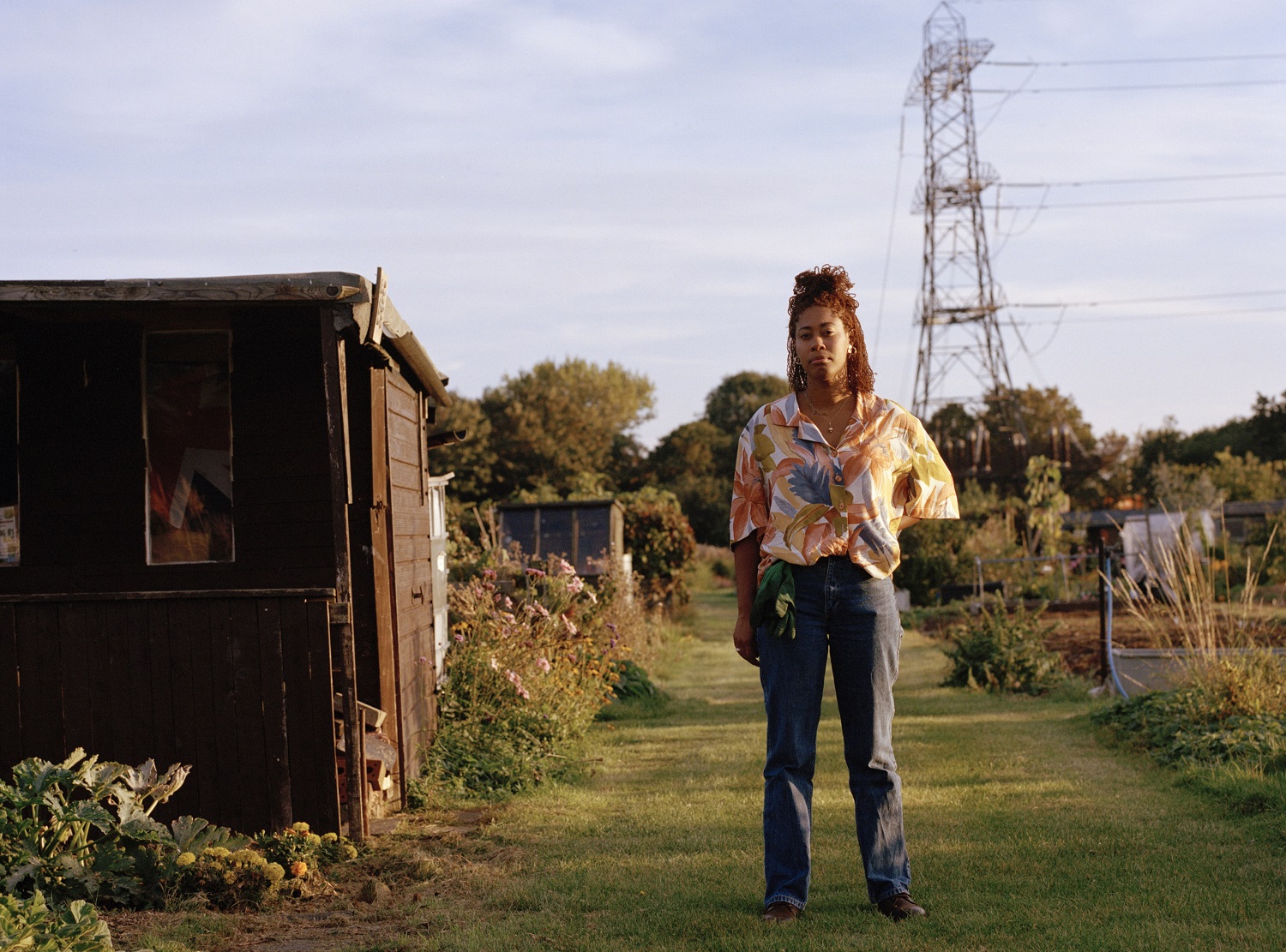 Woman stands outside next to a shed in an alotment space.