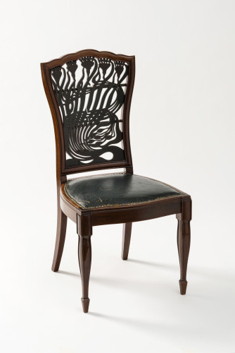 A wooden chair with four legs, a leather seat and an intricate fretwork back