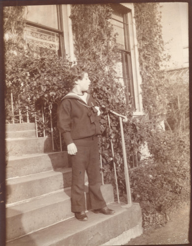 A child stands on the steps of a building covered in foliage