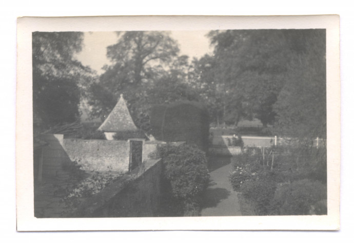 A black and white image of a walled garden with trees behind