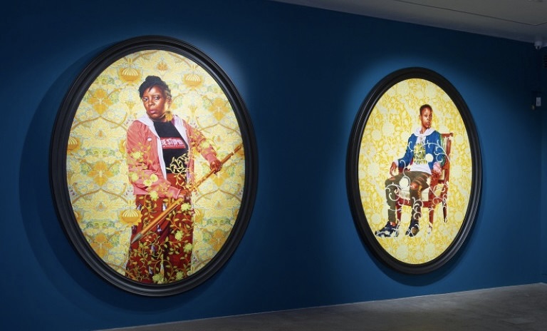 Two brightly coloured portraits of solo females are mounted on dark blue walls