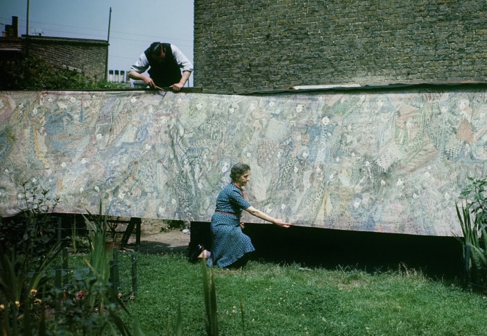 Madge Gill is pictured outside in front of her work. A figure leans over the artwork above her